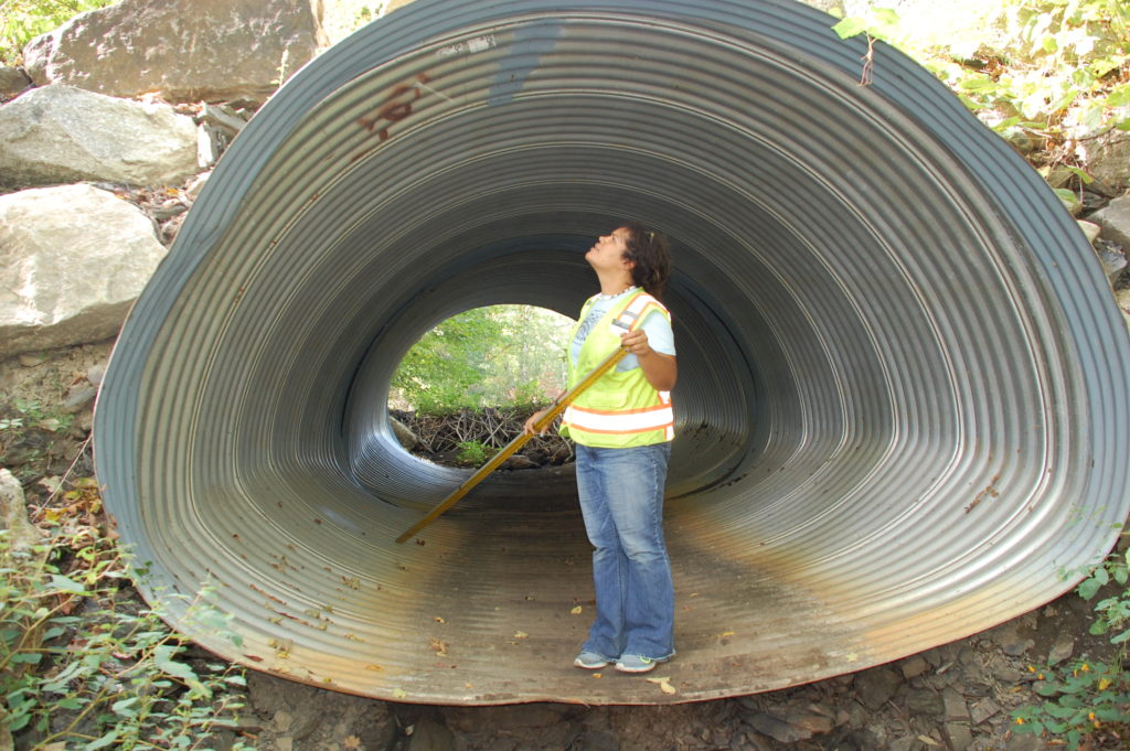 Analyst standing inside large culvert holding measuring rod