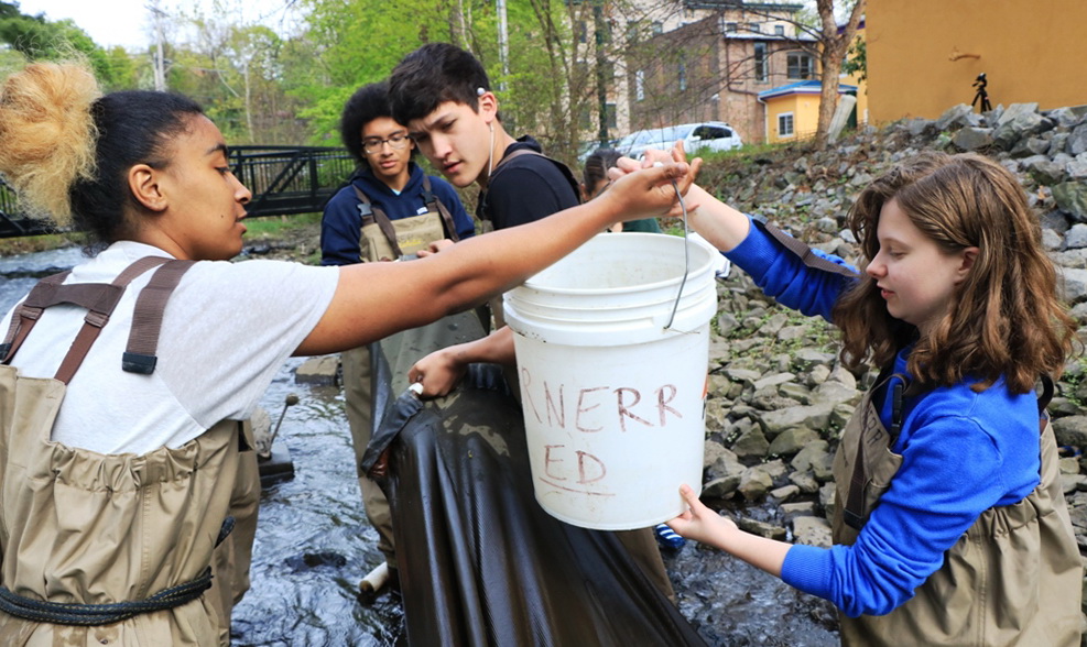 Four youths in a tributary hoisting a large white bucket