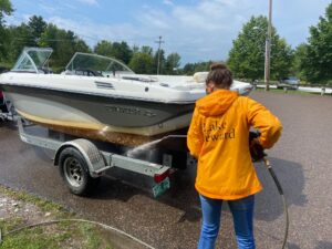 A Boat Launch Steward hosing down a boat on a trailer to remove invasive species