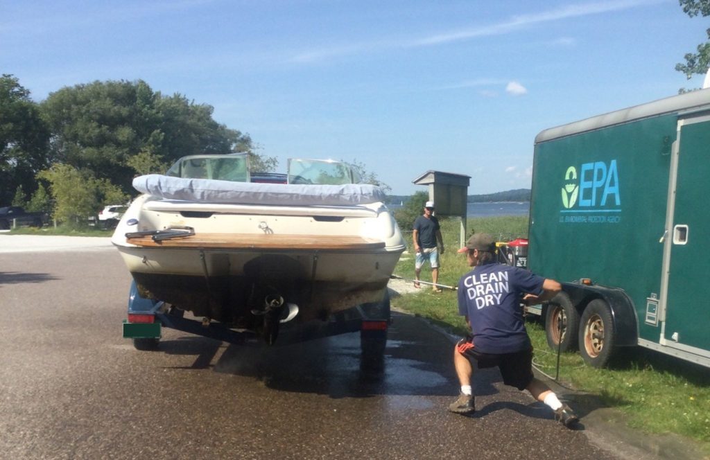 A Lake Champlain boat steward inspecting and cleaning a boat with a "Clean, Drain, Dry" Tshirt.