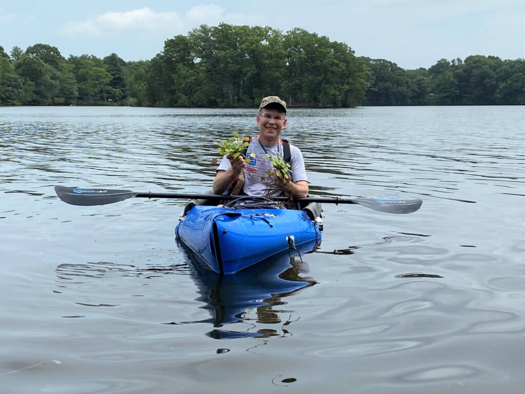 Man with a hat in a kayak holding water chestnut plants.