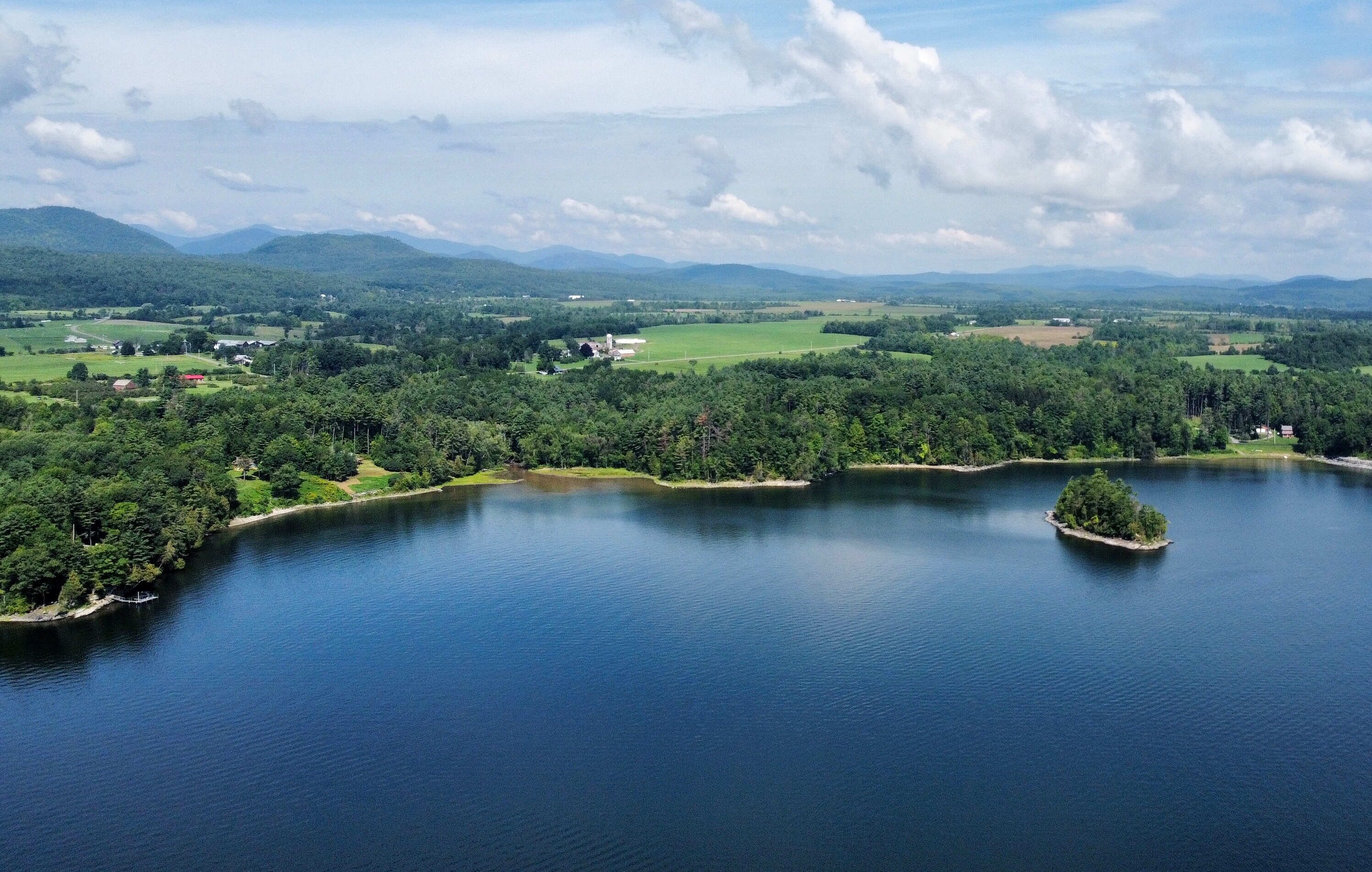 Aerial view of Lake Champlain in the summer with farmlands and mountains in the distance.