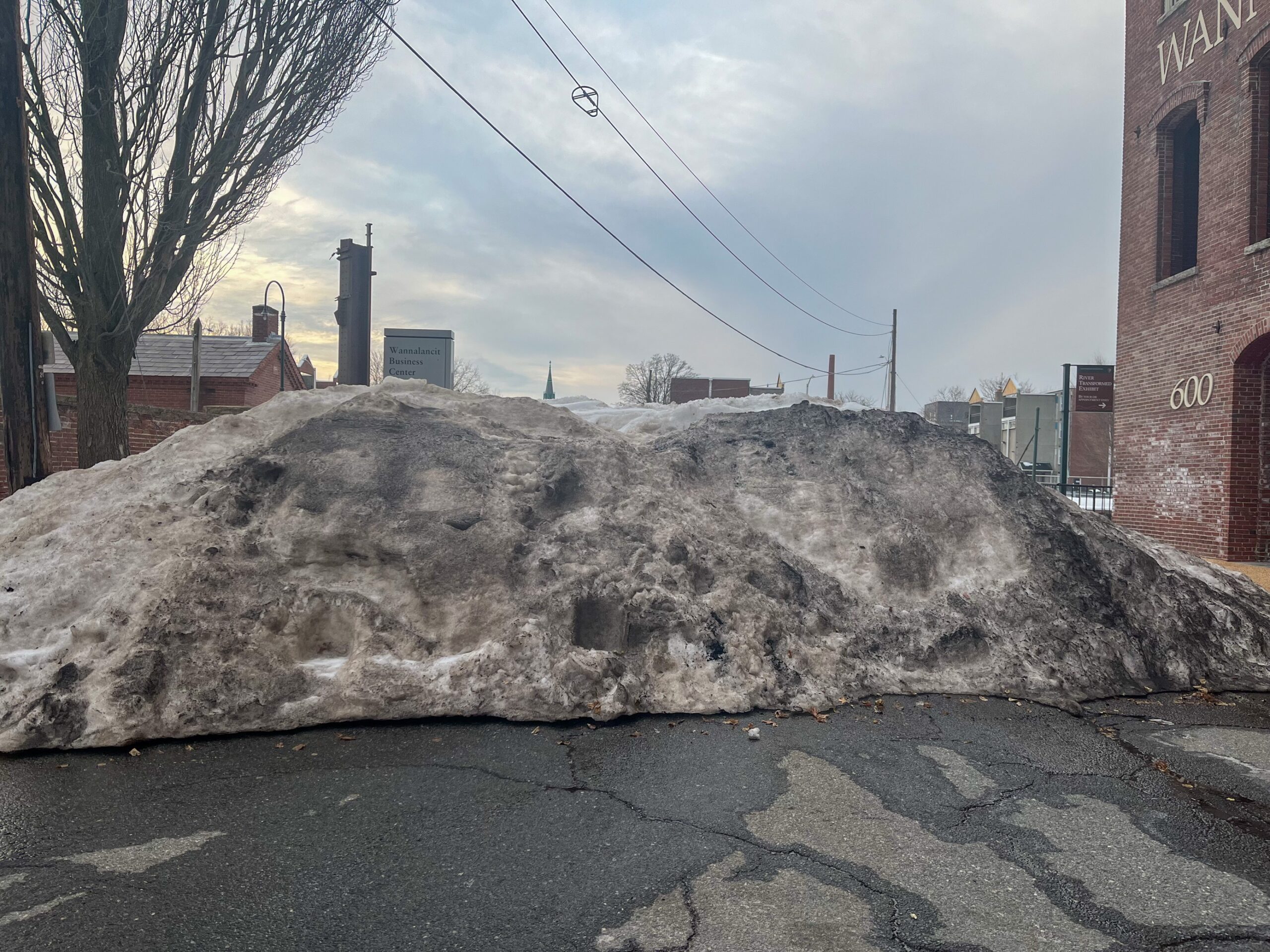 Snow pile located on concrete in an urban area. The snow is tinted black and brown from pollutants.