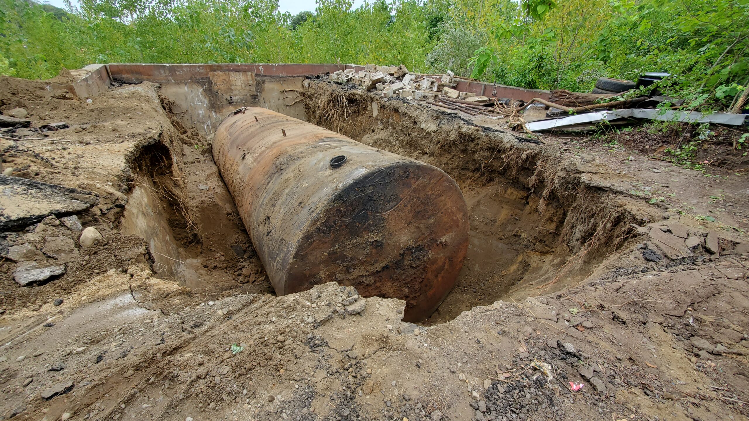 An underground storage tank that has been dug up sits in a hole in the soil.