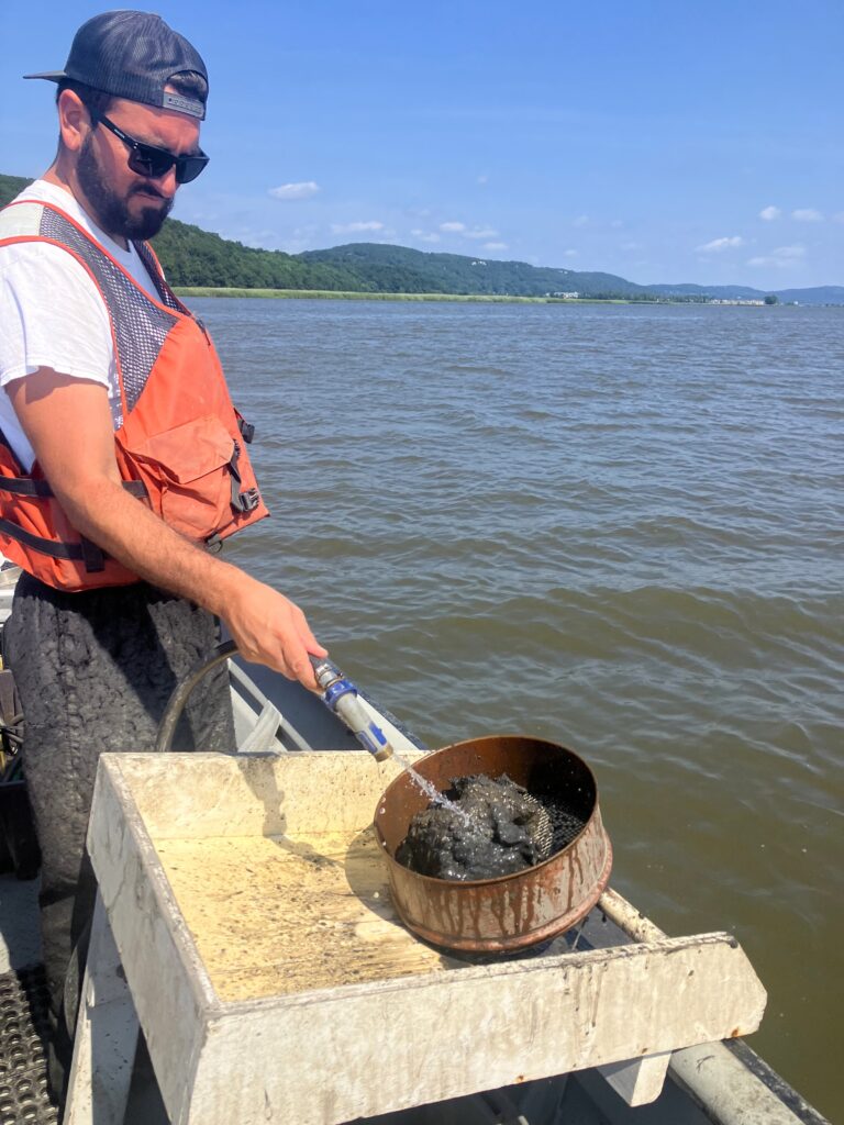 Researchers on a boat wash the sediment in a sieve to remove the fine silts, leaving behind larger objects.
