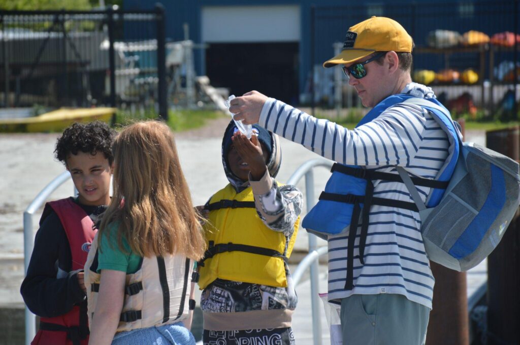 Teacher with three students with PFDs on looking at a water sample.