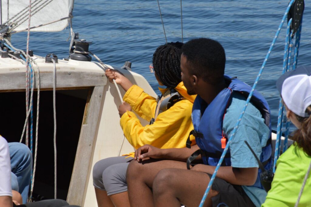 Two youth on a boat, one pulling on a rope and wearing a yellow coat.