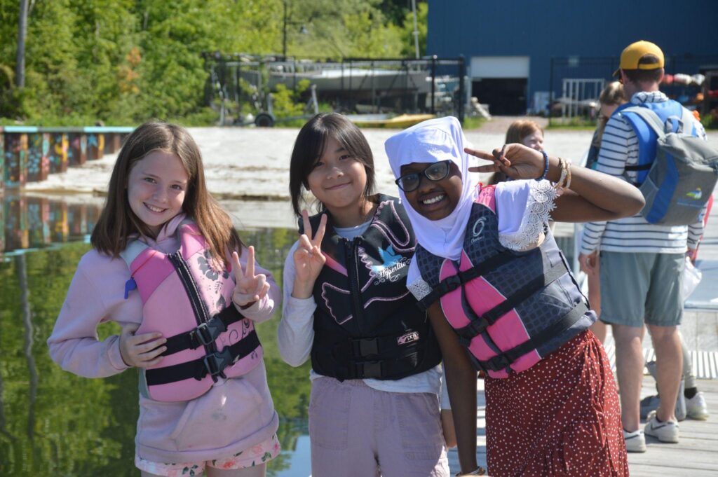Three girls with PFDs on smile for the camera.