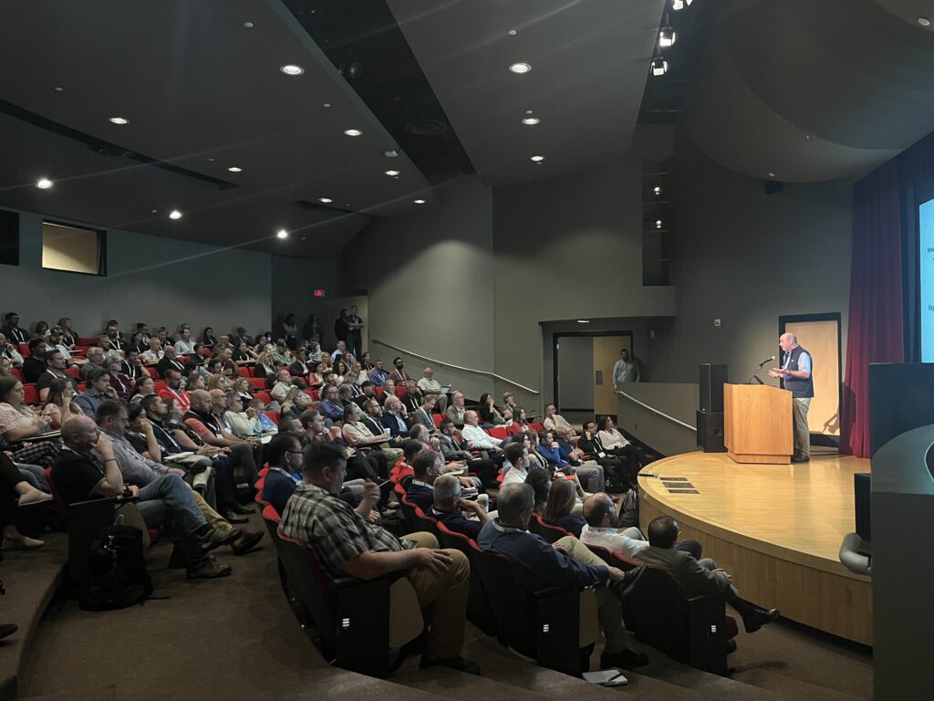 An auditorium with a full audience and a speaker on stage,
