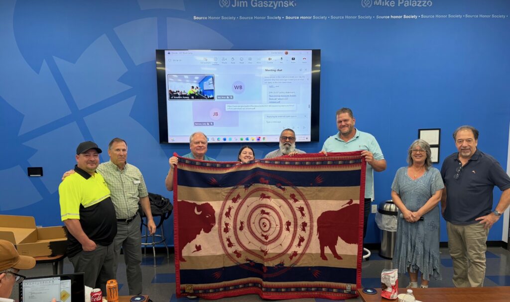 A group of people holding a quilt with buffalo up in front of a screen.