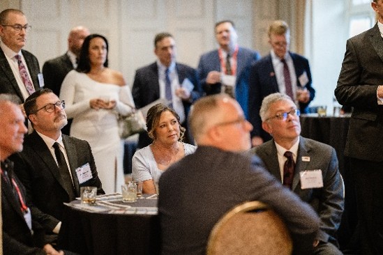 A room of people in business attire at a conference looking up towards a speaker.