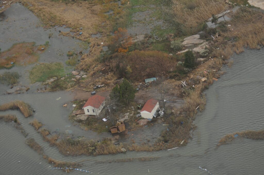 An aerial image showing a house that has been displaced by Hurricane Sandy. Litter is strew about nearby and the water is reaching all the way to where the house is.