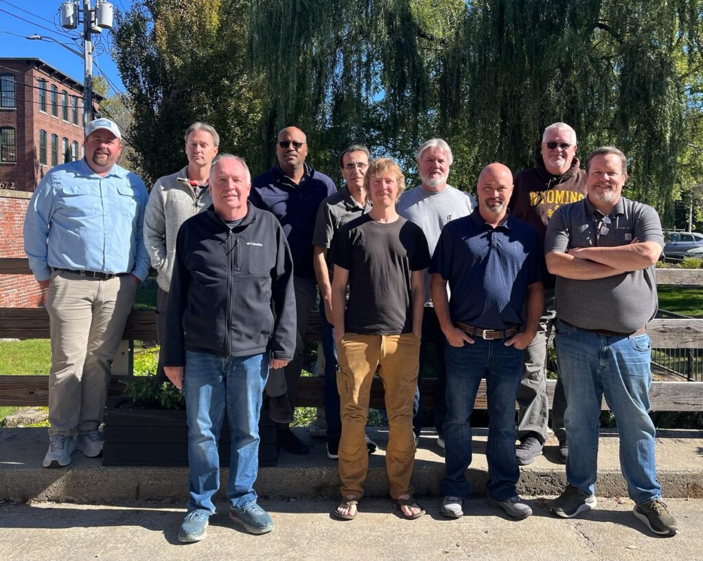 Group of 10 members who make up NWGLDE standing outside in front of a tree